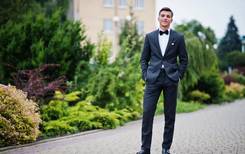 Portrait of a handsome young man in formal fancy suit posing on the pavement in the park on a prom day.