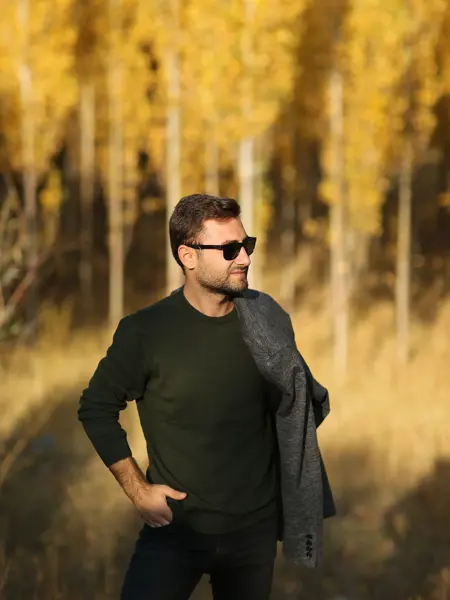 Mann i grønn genser og solbriller poserer ute i gul åker