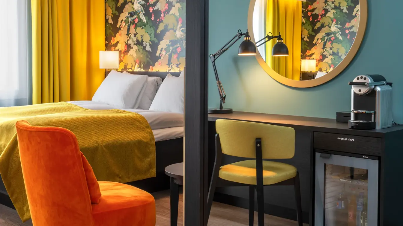 Stort vegghengt speil og oransje stol. Gule gardiner, fargerik tapet og seng med gult sengeteppe i superior room på Thon Hotel Bristol Bergen