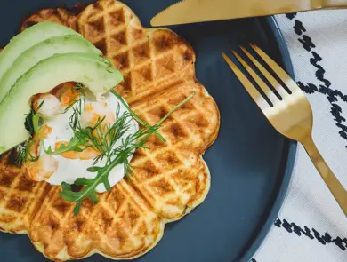 Vafler med avokado og rekesalat på et blått fat ved siden av gullbestikk