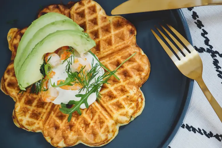 Vafler med avokado og rekesalat på et blått fat ved siden av gullbestikk