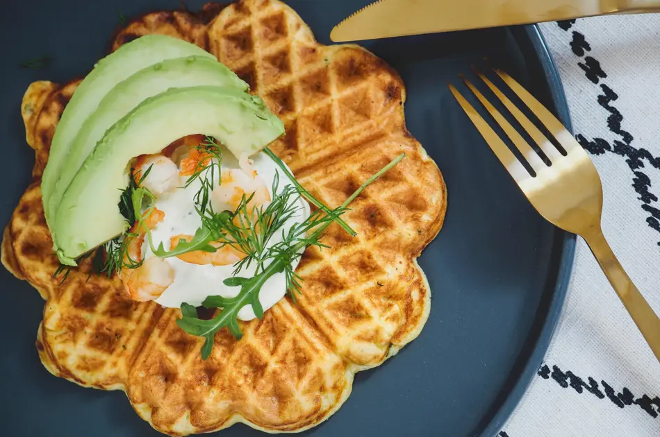 Vafler med avokado og rekesalat på et blått fat ved siden av gullbestikk