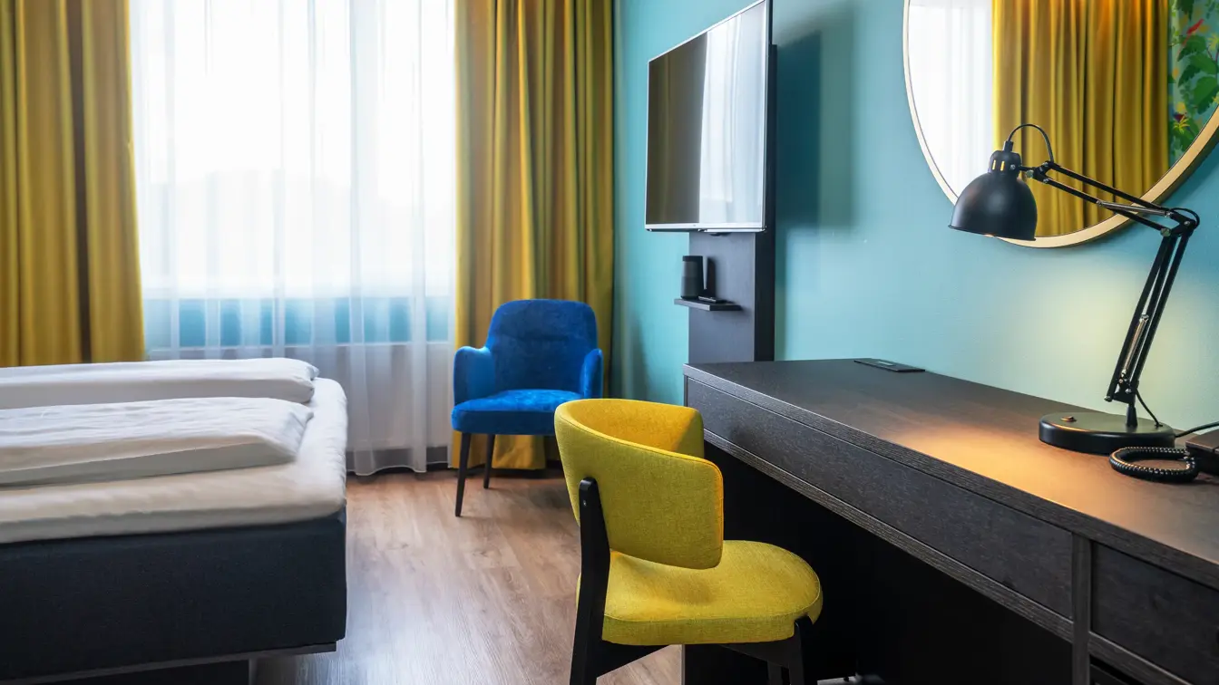 Bå vegg, gule gardiner, dobbeltseng, parkettgulv, blå stol, skrivebord, vindu, gul stol