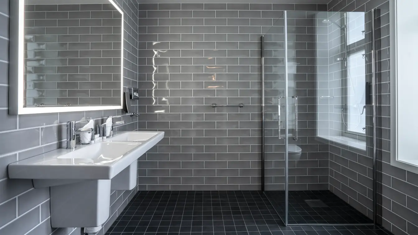 Grå veggfliser, veggspeil, dusj, vask, svarte gulvfliser, vindu 