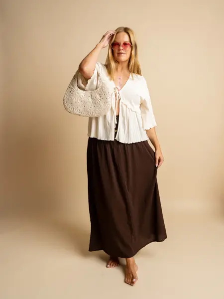 Damemodelle med rosa solbriller, hvit topp, brunt skjørt og hvit heklet veske.