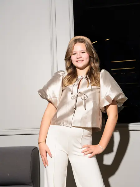 Jente i champagnefarget topp som smiler mot kamera