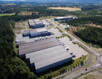 Dronebilde av stort lager- og logistikklokale, med rundkjøring og frodige omgivelser.
