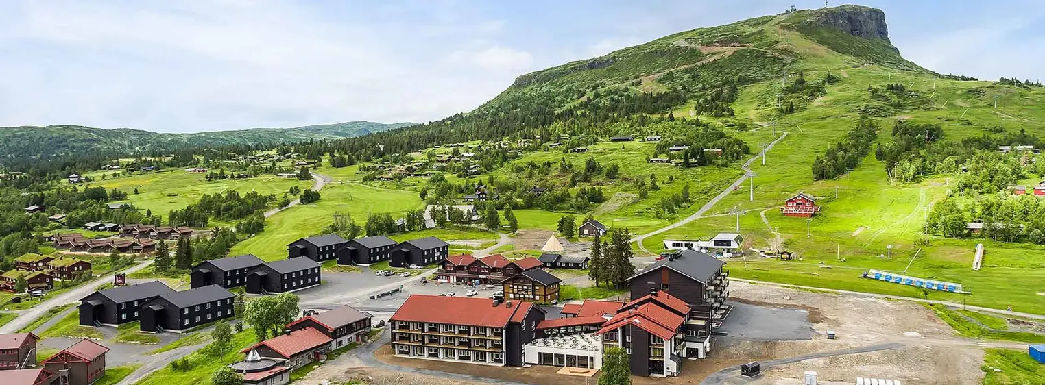 Oversiktsbilde over Høyfjellstunet på Skeikampen man ser bygninger i forgrunnen og det flotte fjellet Skeikampen i bakgrunnen.