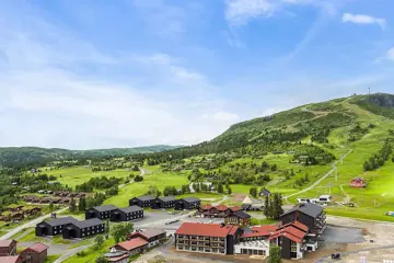 Oversiktsbilde over Høyfjellstunet på Skeikampen man ser bygninger i forgrunnen og det flotte fjellet Skeikampen i bakgrunnen.