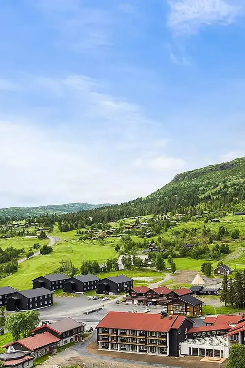 Oversiktsbilde over Høyfjellstunet på Skeikampen man ser bygninger i forgrunnen og det flotte fjellet Skeikampen i bakgrunnen.