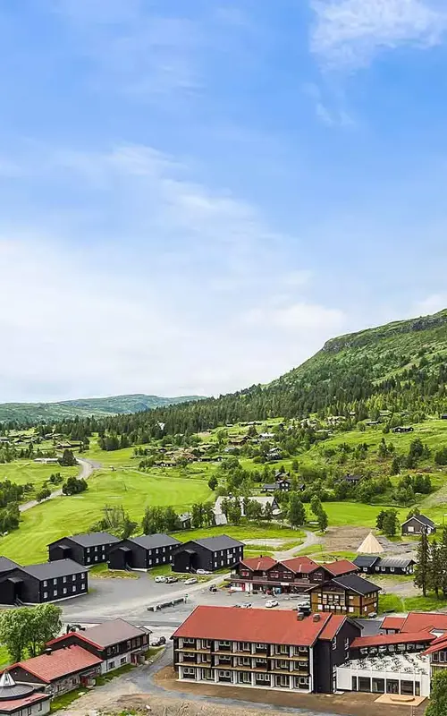 Oversiktsbilde over Høyfjellstunet på Skeikampen man ser bygninger i forgrunnen og det flotte fjellet Skeikampen i bakgrunnen.