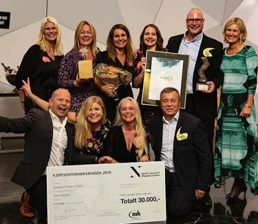 Gruppeabilde av ansatte på AMFI Madla som jubler til kamera mens de holder diplom og stor premiesjekk.