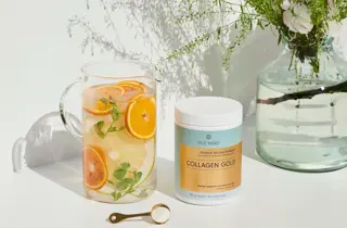 En boks med Collagen Gold fra Vild Nord står ved siden av et glass med vann og skiver av appelsin og sitron.