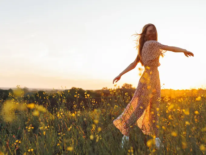 Dame med lang blomstrete kjole danser i gul blomstereng i vårsol 