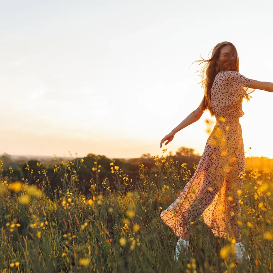 Dame med lang blomstrete kjole danser i gul blomstereng i vårsol 