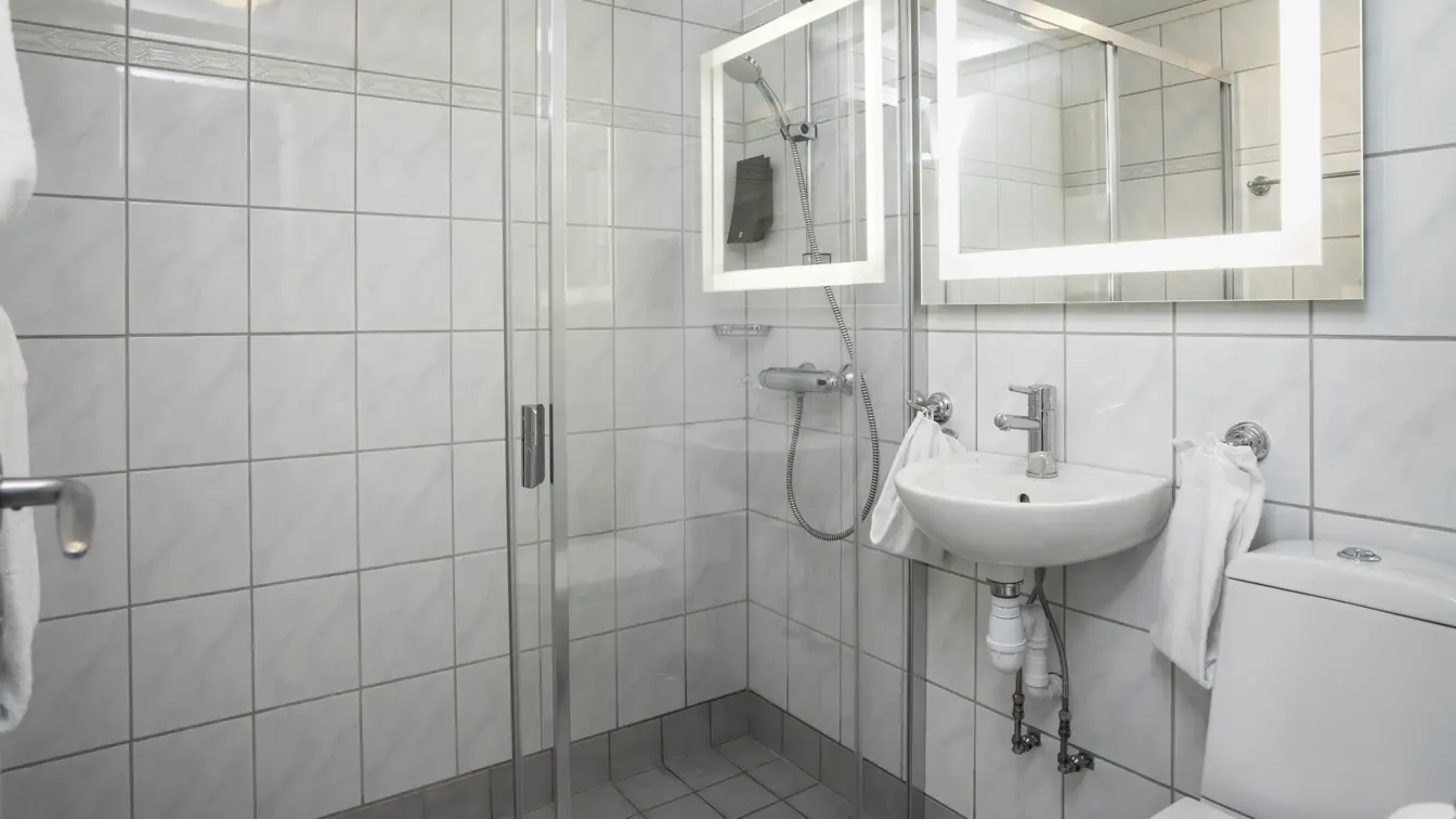 Hvite veggfliser, toalett, speil, vask, dusj. 