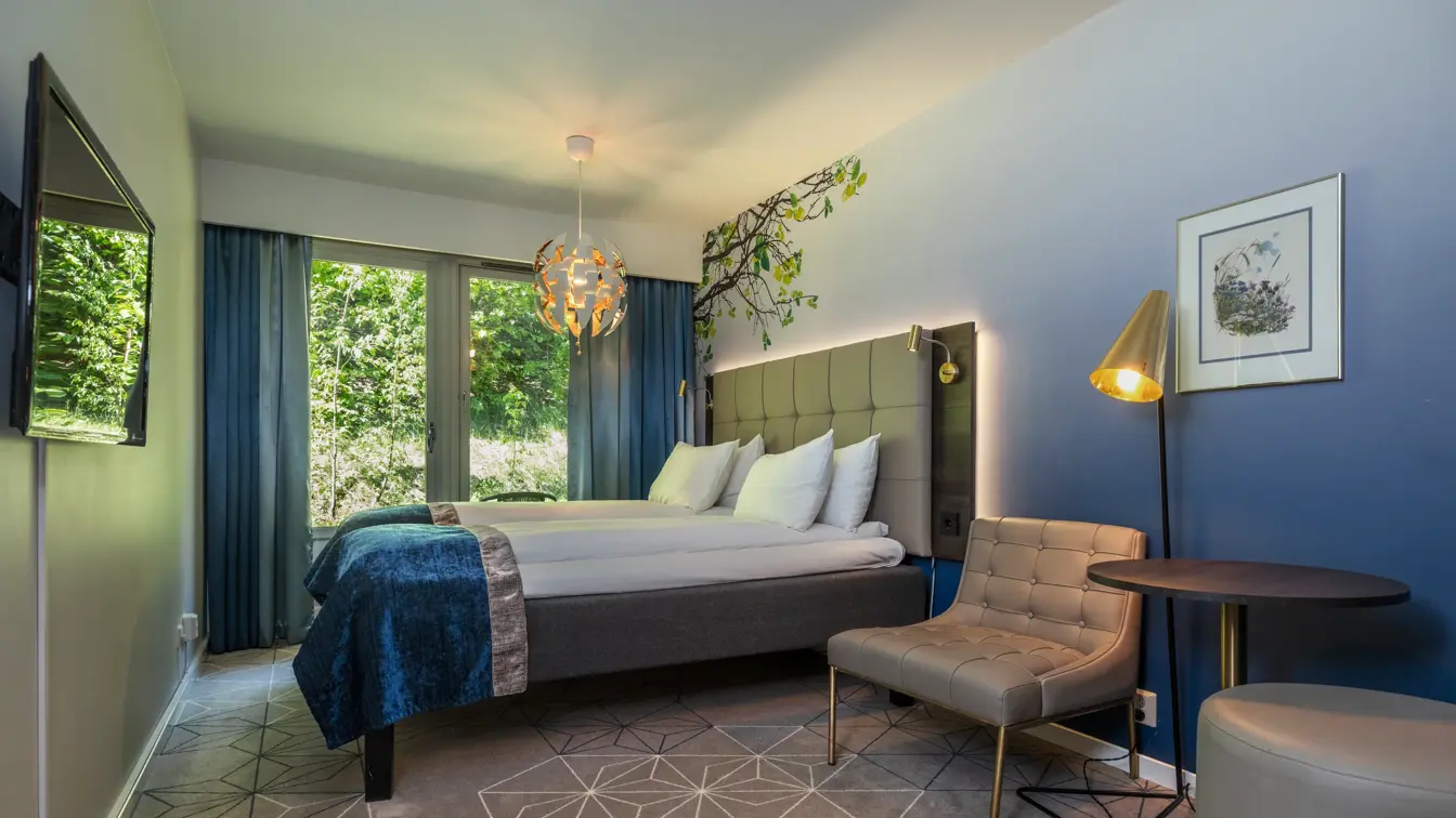 Superior rom med dobbeltseng, blått sengeteppe, gulvteppe, blå vegg, lenestol, store vinduer med blå gardiner