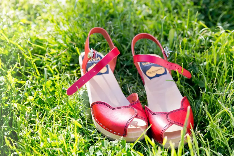 Nærbilde av røde tresko med åpen tå liggende i gress