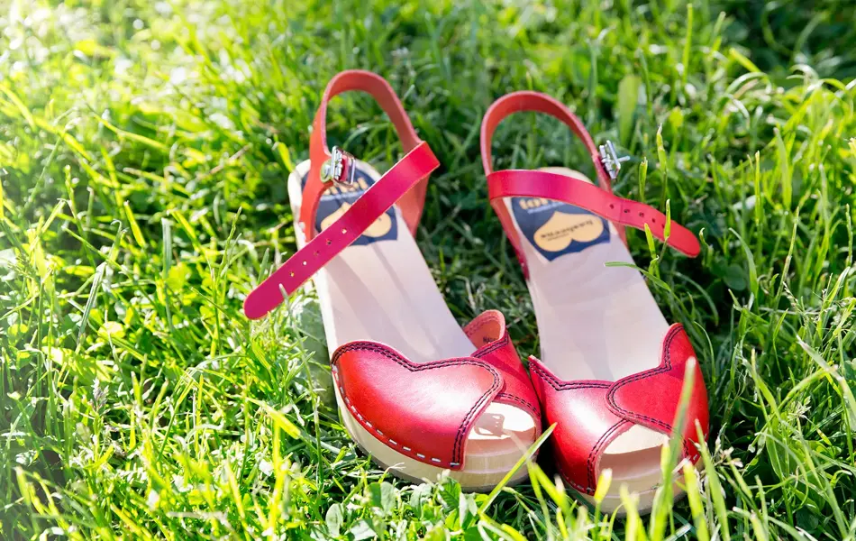 Nærbilde av røde tresko med åpen tå liggende i gress