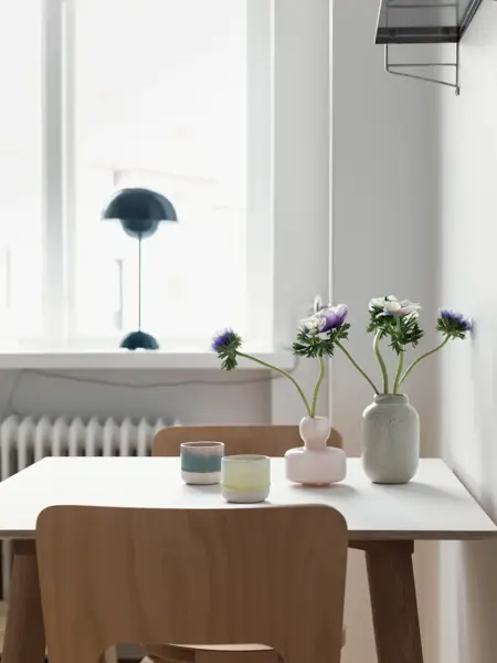 Spisebord med trestoler og mørk blå flowerpotlampe i vinduskarmen 