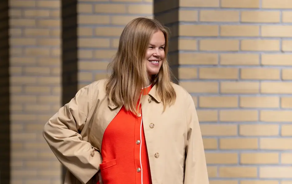 Dame med beige knelangt skjørt, rød topp og beige kort trenchjakke.