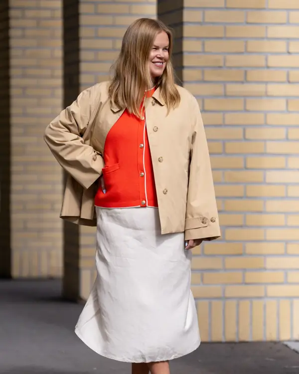 Dame med beige knelangt skjørt, rød topp og beige kort trenchjakke.