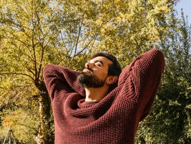 Mann med burgunder ullgenser ser mot sola med høstlig bakgrunn 