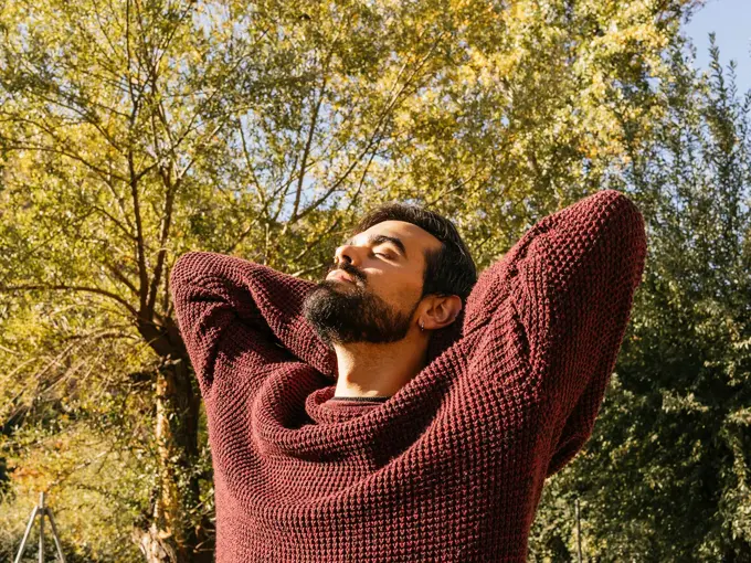 Mann med burgunder ullgenser ser mot sola med høstlig bakgrunn 