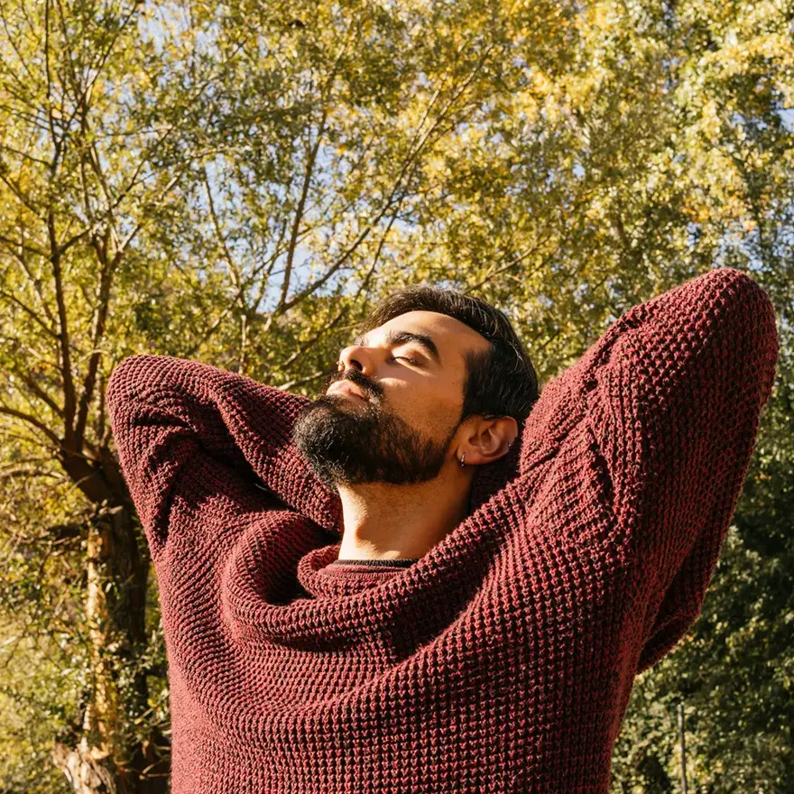 Mann med burgunder ullgenser ser mot sola med høstlig bakgrunn 