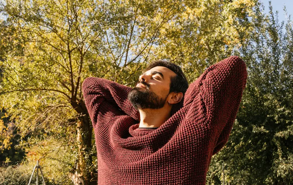 Mann med burgunder ullgenser ser mot sola med høstlig bakgrunn 