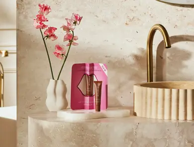 Rituals leppepleiesett i gaveeske plassert ved en vask med blomster i bakgrunnen.