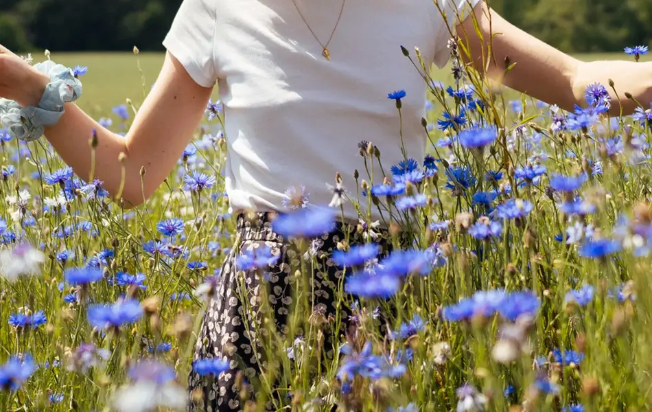 Smilende dame med hvit bøttehatt i blomstereng 