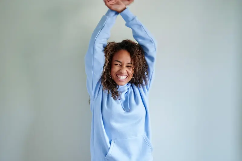 Dame med lys blå hettegenser danser foran dus blå vegg 