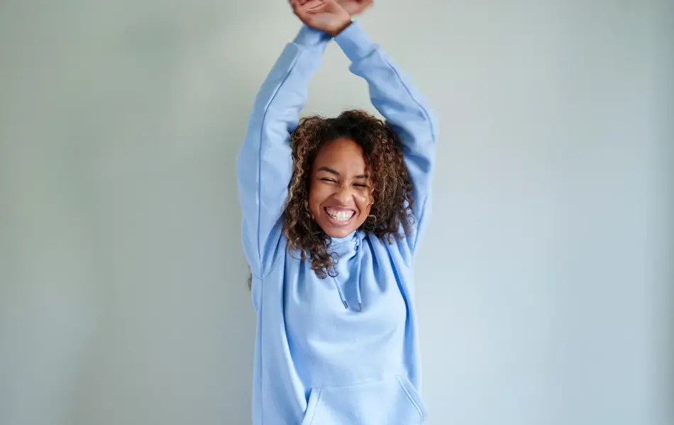 Dame med lys blå hettegenser danser foran dus blå vegg 