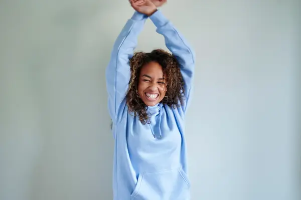 Dame med lys blå hettegenser danser foran dus blå vegg 