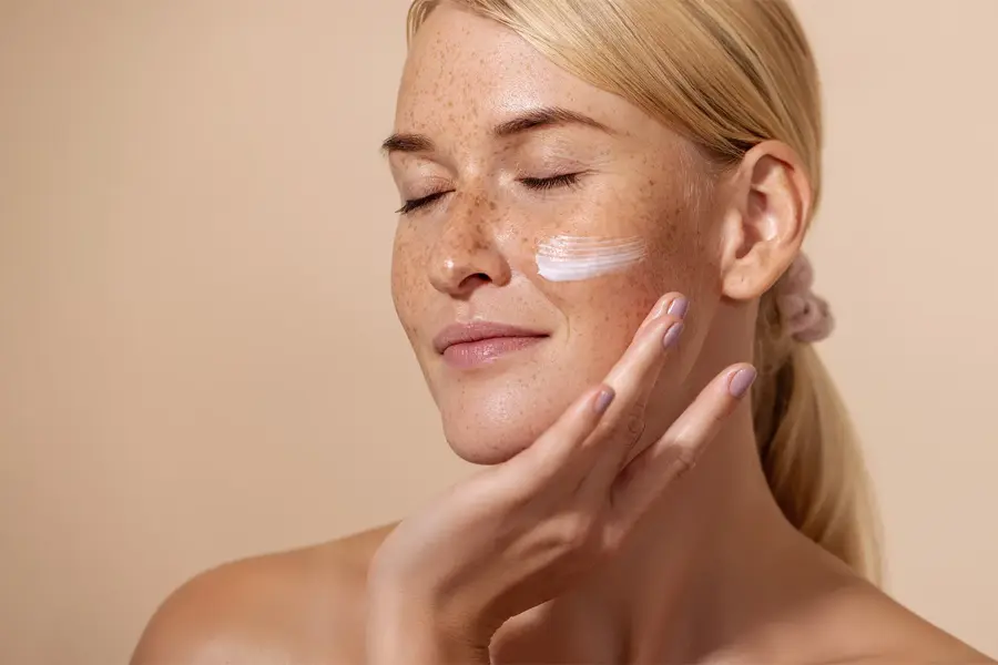 Dame med lyst hår, fregner som har smørt på krem på ansiktet