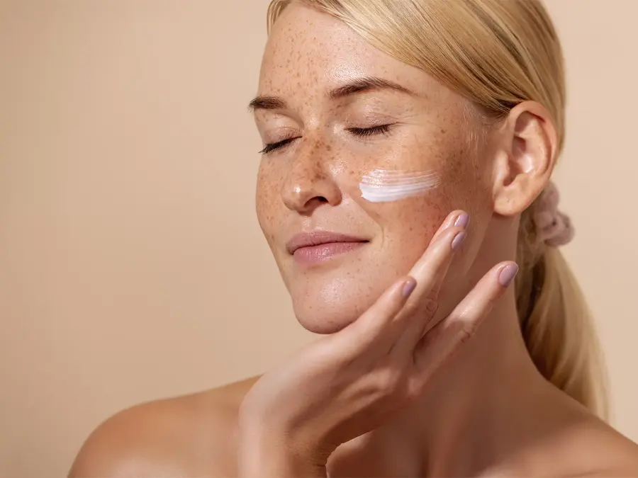 Dame med lyst hår, fregner som har smørt på krem på ansiktet