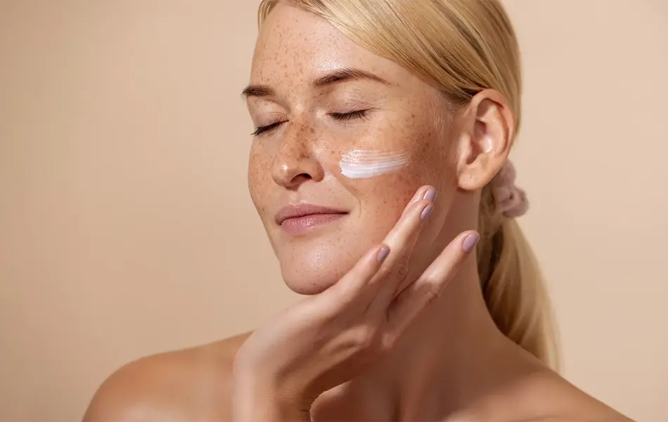 Dame med lyst hår, fregner som har smørt på krem på ansiktet