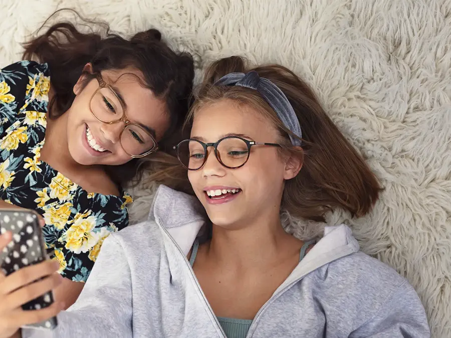 to unge jenter med briller som ligger på gulvet med mobil i hånden