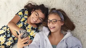 to unge jenter med briller som ligger på gulvet med mobil i hånden