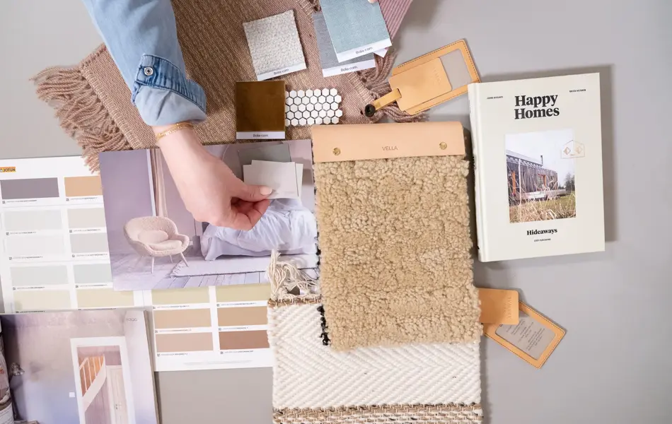 En dame som holder på med oppussing og tips om interiør trender for våren 2021. Damen har lyst halvlangt hå og har på seg en blå olaskjorte og blå olabukse. Fargene går i brunt og beige jordtoner og det er mye lilla og pastellfarger. Vårens interiør