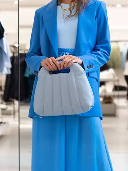 Nærbilde av ung kvinne i blå dress som holder en lyseblå veske