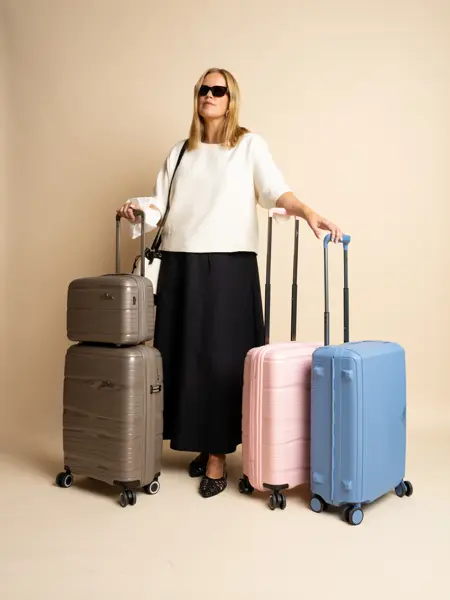 Dame modelle med sorte solbriller, hvit genser, sort skjørt og sorte sko, står med tre tillekofferter.