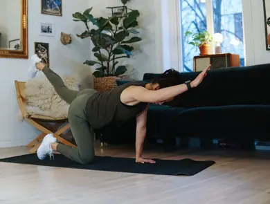 treningsekspert Anna Johansen trener på matte på gulvet, mørkegrønn sofa i bakgrunnen, lys stol med pels oppi, str grønn plante, bilder på veggen