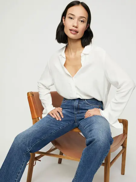 kvinnelig modell som sitter på stol iført hvit bluse og jeans