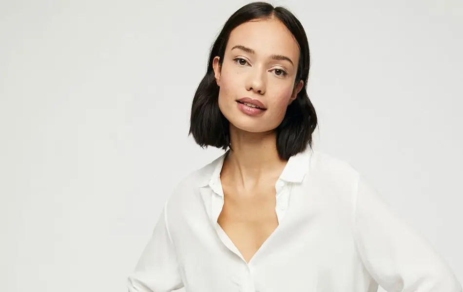 kvinnelig modell som sitter på stol iført hvit bluse og jeans