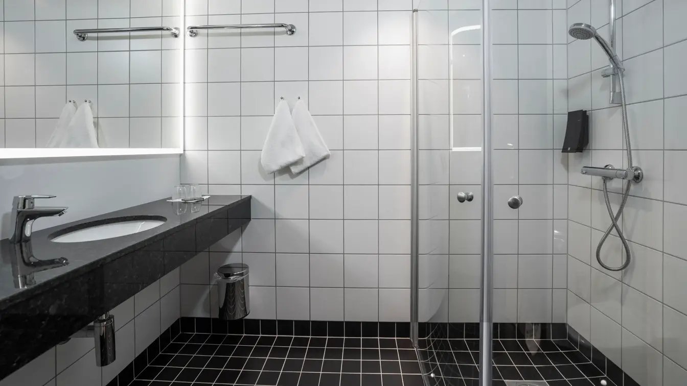 Speil, hvite veggfliser, svart vask, dusj, svarte gulvfliser