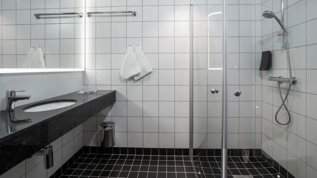 Speil, hvite veggfliser, svart vask, dusj, svarte gulvfliser