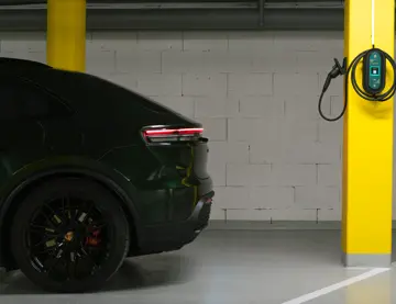En mørk el-bil står i en garasje, og en lader er montert på en gul søyle.
