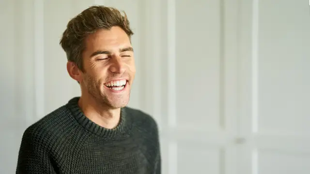 Mann i grønn ullgenser ler 